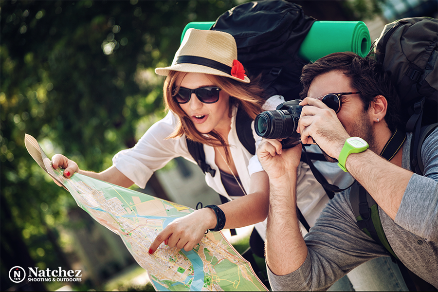 A young couple of backpackers, the woman looking at a map, the man taking a picture of nature?