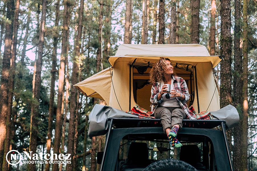 A woman drinking coffee on the roof of her vehicle against a car rooftop tent?