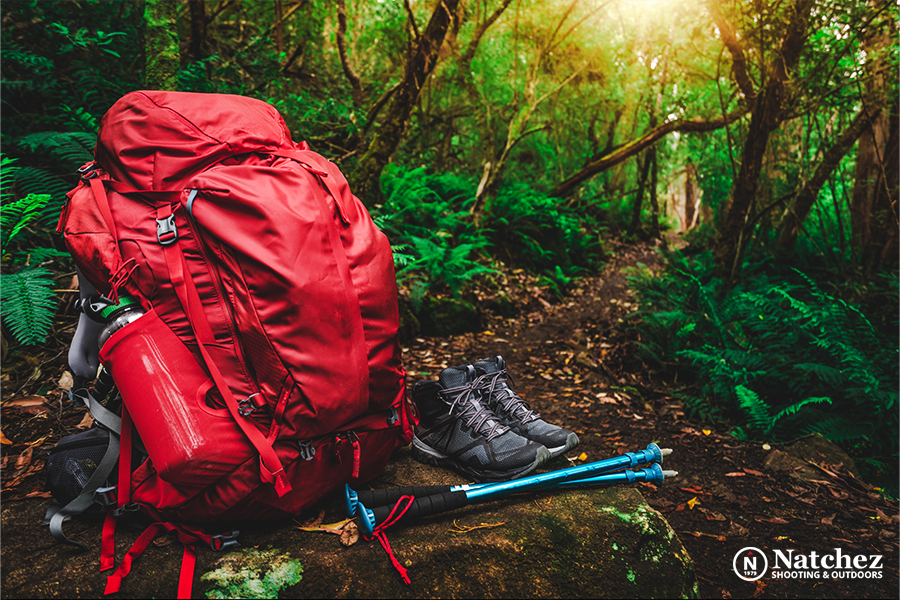 A red backpack, trekking poles and hiking footwear in the forest?