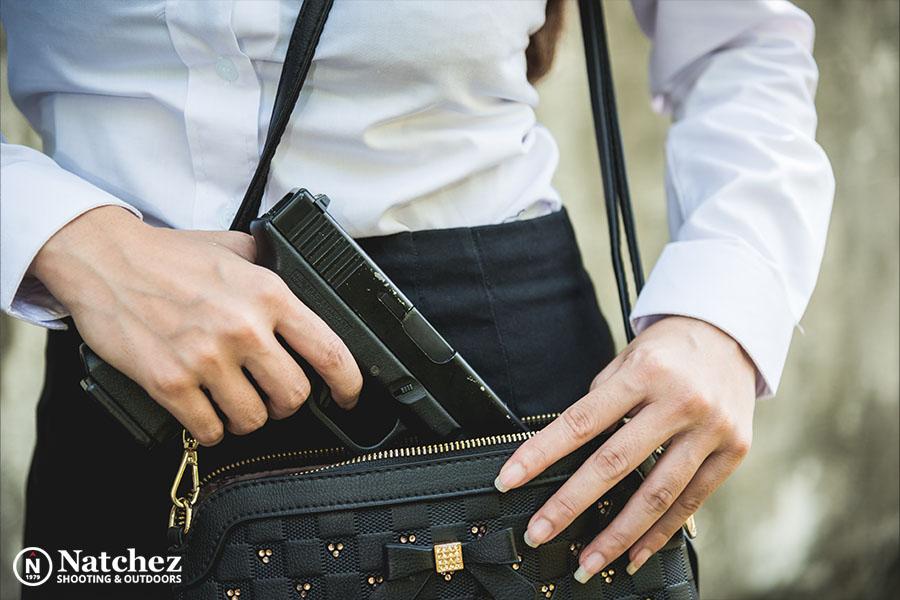 9mm pistol in a womans hand being removed from concealed carry purse